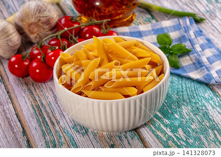 Penne pasta in white bowl with cherry tomatoes garlic and basil on rustic wooden table 141328073