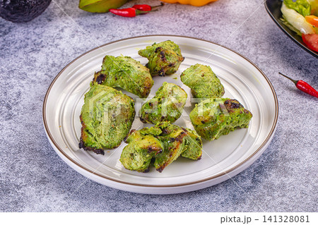 Green herb coated chicken tikka pieces on white plate with chili peppers and avocado 141328081