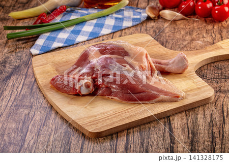 Raw duck leg on wooden cutting board, fresh ingredients for cooking, rustic kitchen setting, gourmet cuisine preparation Raw duck leg on wooden cutting board, fresh ingredients for cooking, rustic kitchen setting, gourmet cuisine preparation 141328175