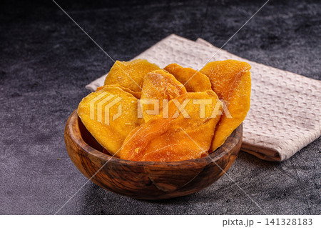 Dried mango slices in wooden bowl on dark textured surface 141328183