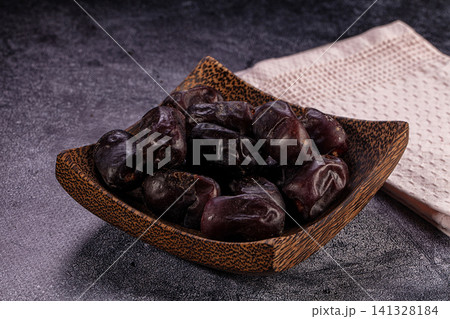 Dark dates in wooden bowl on textured surface Dark dates in wooden bowl on textured surface 141328184
