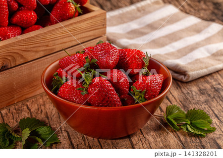 Fresh strawberries in ceramic bowl on rustic wooden table 141328201