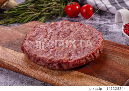 Raw beef burger patty on wooden cutting board with rosemary and cherry tomatoes Raw beef burger patty on wooden cutting board with rosemary and cherry tomatoes 141328244