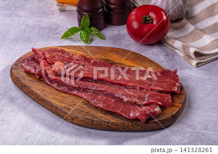 Raw beef steak slices on wooden cutting board with tomato basil garlic Raw beef steak slices on wooden cutting board with tomato basil garlic 141328261