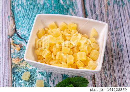 Dried pineapple chunks in white bowl on rustic wooden surface with mint leaves Dried pineapple chunks in white bowl on rustic wooden surface with mint leaves 141328279