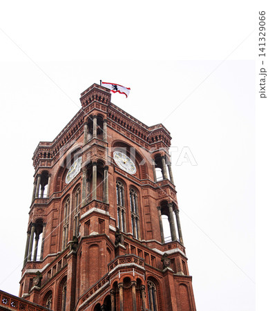 Berlin red town hall with Berlin flag flying in the cloudy sky. Detailed view of Rotes Rathaus clock tower, iconic landmark featuring ornate brickwork representing the city history. Copy space 141329066