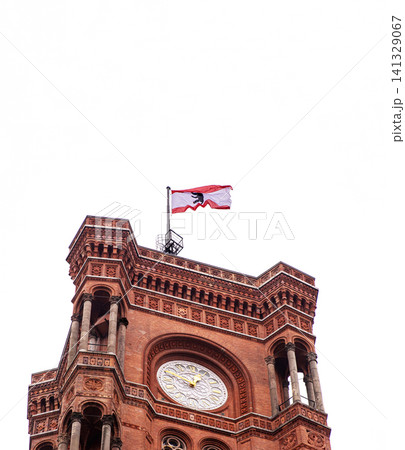 Berlin red town hall with Berlin flag flying in the cloudy sky. Detailed view of Rotes Rathaus clock tower, iconic landmark featuring ornate brickwork representing the city history. Copy space 141329067