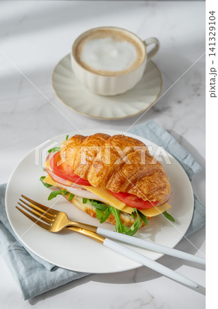 A golden croissant sandwich with ham, cheese, tomato, and arugula on a marble background 141329104