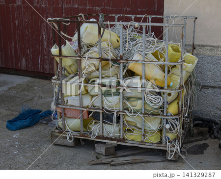 Colorful vintage yellow plastic buoys and marine ropes are stacked in a weathered metal cage at a fishing shipyard. The scene shows the busy environment of fishing work. Colorful vintage yellow plastic buoys and marine ropes are stacked in a weathered metal cage at a fishing shipyard. The scene shows the busy environment of fishing work. 141329287