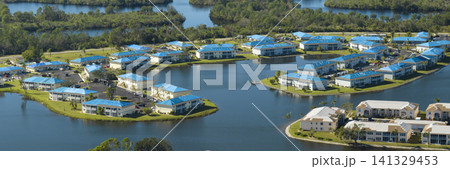 Aerial view of damaged in hurricane apartment building roofs covered with blue protective tarp against rain water leaking until replacement of asphalt shingles Aerial view of damaged in hurricane apartment building roofs covered with blue protective tarp against rain water leaking until replacement of asphalt shingles 141329453