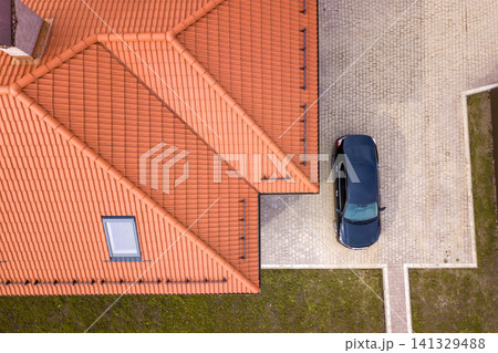 Aerial top view of house metal shingle roof with attic windows and black car on paved yard. Aerial top view of house metal shingle roof with attic windows and black car on paved yard. 141329488