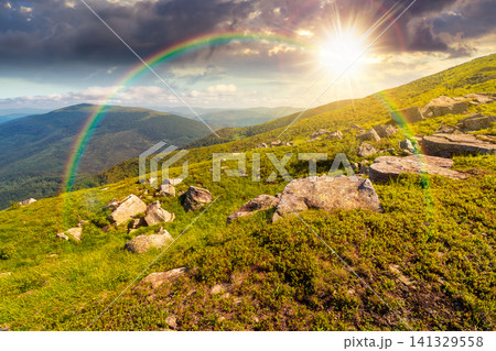 sunset over mountain landscape with grass and rock on a slope. view in to the distant valley of carpathian mountains. mountainous scenery of ukraine in summer. weather with rainbow sunset over mountain landscape with grass and rock on a slope. view in to the distant valley of carpathian mountains. mountainous scenery of ukraine in summer. weather with rainbow 141329558