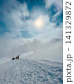 雪雲から差し込む太陽の光と雪山を登る登山者 141329872