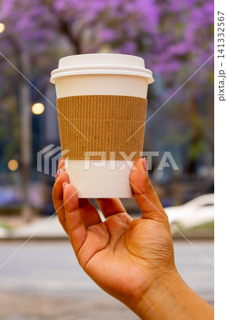 Close up of hand holding a takeaway coffee cup with blooming jacaranda trees Close up of hand holding a takeaway coffee cup with blooming jacaranda trees 141332567