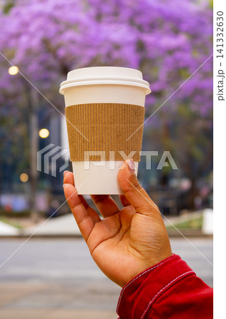 Hand holding a take away coffee cup with jacaranda trees in the background Hand holding a take away coffee cup with jacaranda trees in the background 141332630