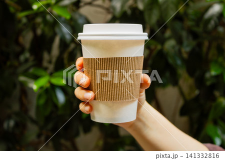 Hand holding a takeaway coffee cup with green leaves horizontal background Hand holding a takeaway coffee cup with green leaves horizontal background 141332816
