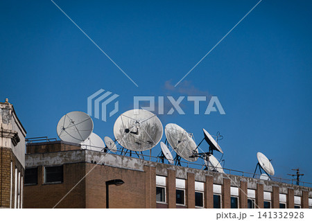 Parabolic antennas designed to receive or transmit radio wave information. They are mounted on a brick building under a clear blue sky Parabolic antennas designed to receive or transmit radio wave information. They are mounted on a brick building under a clear blue sky 141332928