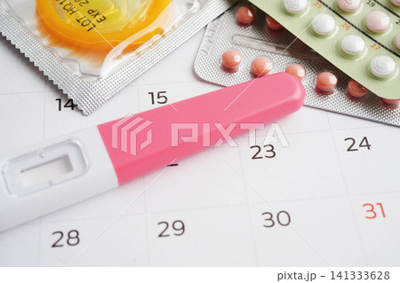 Pregnancy test with birth control pills and condom for female on calendar, ovulation day. Pregnancy test with birth control pills and condom for female on calendar, ovulation day. 141333628