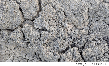 A high angle overhead look captures deeply cracked dry earth, rough gravel textures on the ground surface. The arid soil breaks into unique geometric fractured chunks, showing variations of grey mud, A high angle overhead look captures deeply cracked dry earth, rough gravel textures on the ground surface. The arid soil breaks into unique geometric fractured chunks, showing variations of grey mud, 141334424