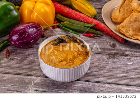 Spicy Indian dal tadka curry in white bowl surrounded by fresh vegetables on rustic wooden table Spicy Indian dal tadka curry in white bowl surrounded by fresh vegetables on rustic wooden table 141335672