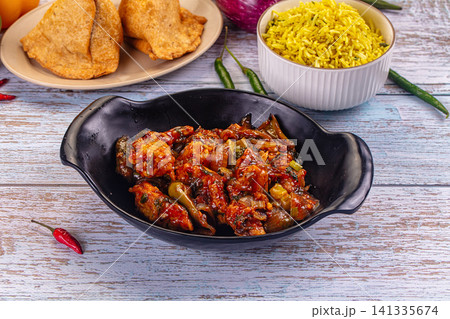 Spicy glazed breaded prawn stir-fry with bell peppers and onions served with yellow rice and fried snacks on rustic wooden table Spicy glazed breaded prawn stir-fry with bell peppers and onions served with yellow rice and fried snacks on rustic wooden table 141335674