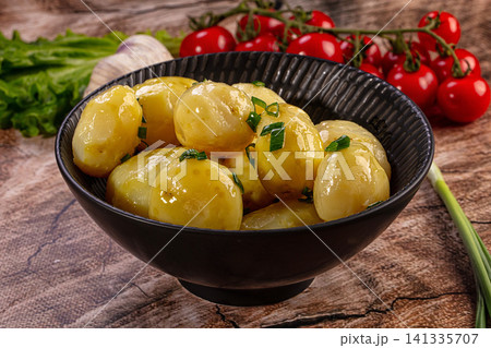 Boiled young potatoes with green onion and butter in a black bowl on a rustic wooden table Boiled young potatoes with green onion and butter in a black bowl on a rustic wooden table 141335707