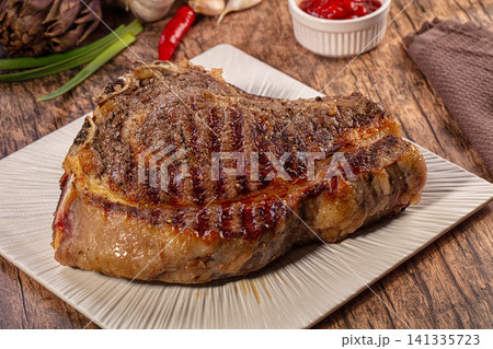 Grilled ribeye steak on textured plate with garlic chili artichoke and ketchup on rustic wood Grilled ribeye steak on textured plate with garlic chili artichoke and ketchup on rustic wood 141335723