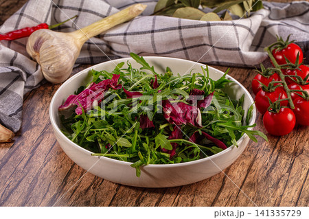 Fresh arugula radicchio salad bowl with cherry tomatoes garlic on rustic wood 141335729