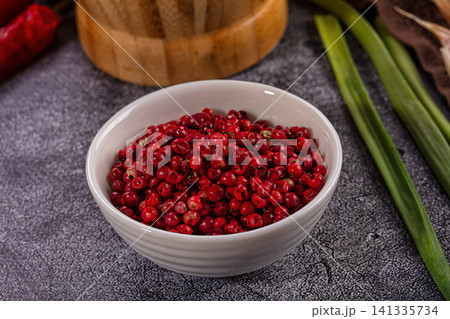 Vibrant red peppercorns in white ceramic bowl with green onions and wooden mortar on dark textured surface Vibrant red peppercorns in white ceramic bowl with green onions and wooden mortar on dark textured surface 141335734