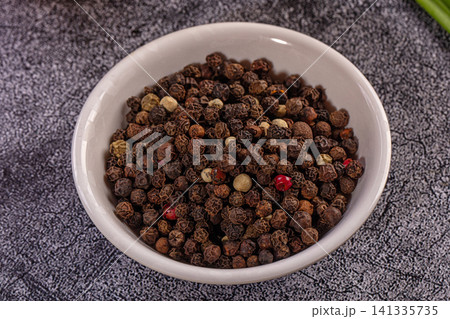 Assorted peppercorns in white bowl on textured gray surface Assorted peppercorns in white bowl on textured gray surface 141335735