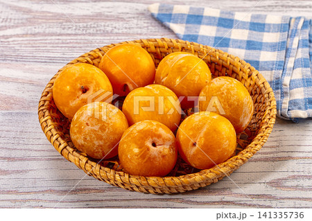 Yellow plums in woven basket on rustic wood with blue checkered cloth 141335736