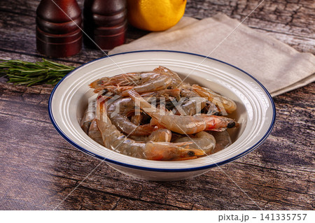 Raw king prawns in white enamel bowl with lemon rosemary on rustic wood 141335757
