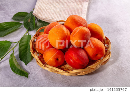 Ripe apricots in woven basket with green leaves on gray fabric Ripe apricots in woven basket with green leaves on gray fabric 141335767