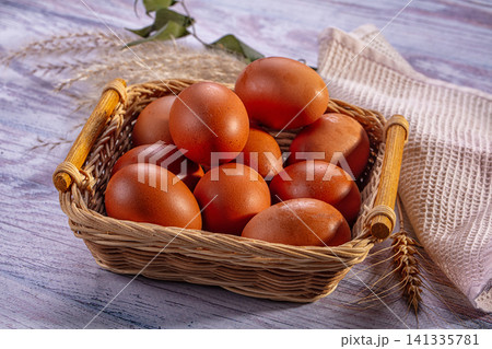 Brown eggs in woven basket on rustic wooden surface with wheat stalks and cloth 141335781