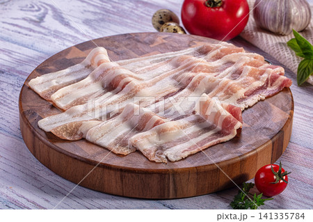 Raw bacon strips on wooden cutting board with tomato garlic and herbs 141335784