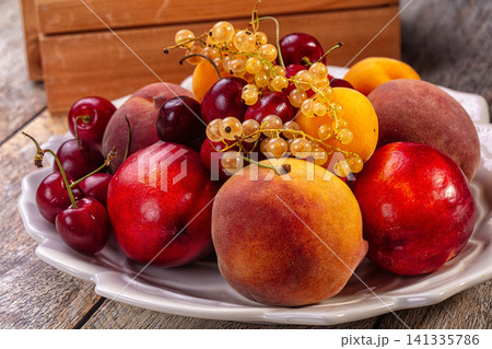 Fresh summer fruit assortment on white plate with wooden background Fresh summer fruit assortment on white plate with wooden background 141335786