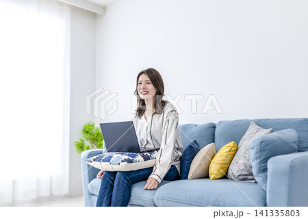 自宅のソファでノートパソコンを使う若い女性 自宅のソファでノートパソコンを使う若い女性 141335803