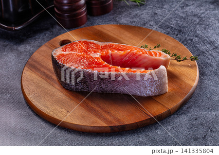 Raw salmon fillet on wooden cutting board with herb garnish 141335804
