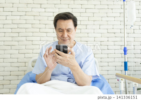 Old man in medical bed making video call to family member while in hospital. Old man in medical bed making video call to family member while in hospital. 141336151