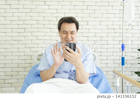 Old man in medical bed making video call to family member while in hospital. Old man in medical bed making video call to family member while in hospital. 141336152