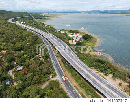 Drone aerial view of a highway running beside a reservoir with lush green mountains, Transportation infrastructure and renewable energy concept 141337347