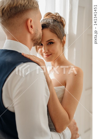 Portrait of a beautiful groom and a bride by the window Portrait of a beautiful groom and a bride by the window 141341451