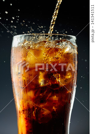 Sparkling cola is poured into a misted glass with ice. Sparkling cola is poured into a misted glass with ice. 141341511
