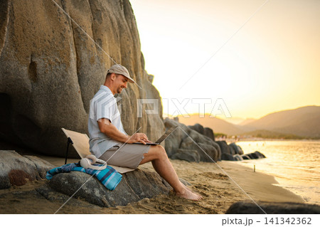 Man working on laptop at beach during sunset in Greece 141342362
