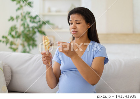 Worried Black pregnant woman examining loose hair in hairbrush at home 141343939