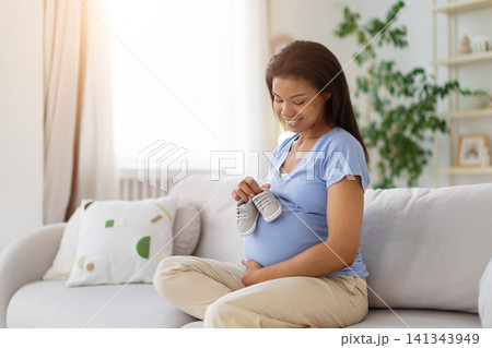 Smiling Black pregnant woman holding tiny newborn shoes above her belly Smiling Black pregnant woman holding tiny newborn shoes above her belly 141343949
