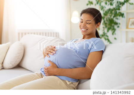 Relaxed Black pregnant woman reclining on soft sofa with eyes closed Relaxed Black pregnant woman reclining on soft sofa with eyes closed 141343992