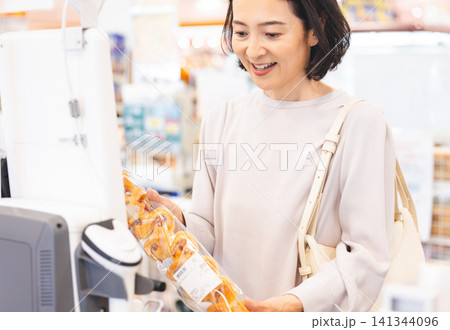 セルフレジで商品のバーコードを読み取る笑顔の女性客 セルフレジで商品のバーコードを読み取る笑顔の女性客 141344096