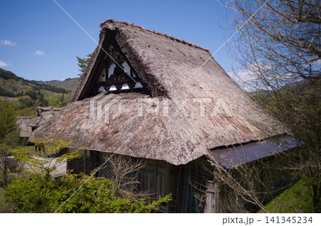 青空と山並みを背景にした合掌造りの茅葺き屋根 妻壁の装飾意匠 青空と山並みを背景にした合掌造りの茅葺き屋根 妻壁の装飾意匠 141345234