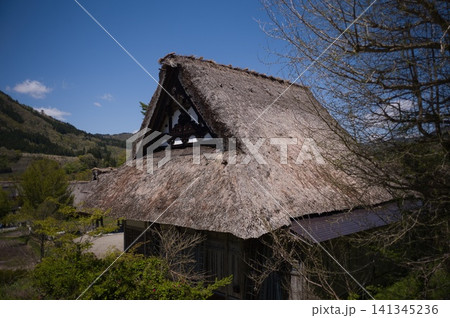 青空と山並みを背景にした合掌造りの茅葺き屋根 妻壁の装飾意匠 青空と山並みを背景にした合掌造りの茅葺き屋根 妻壁の装飾意匠 141345236